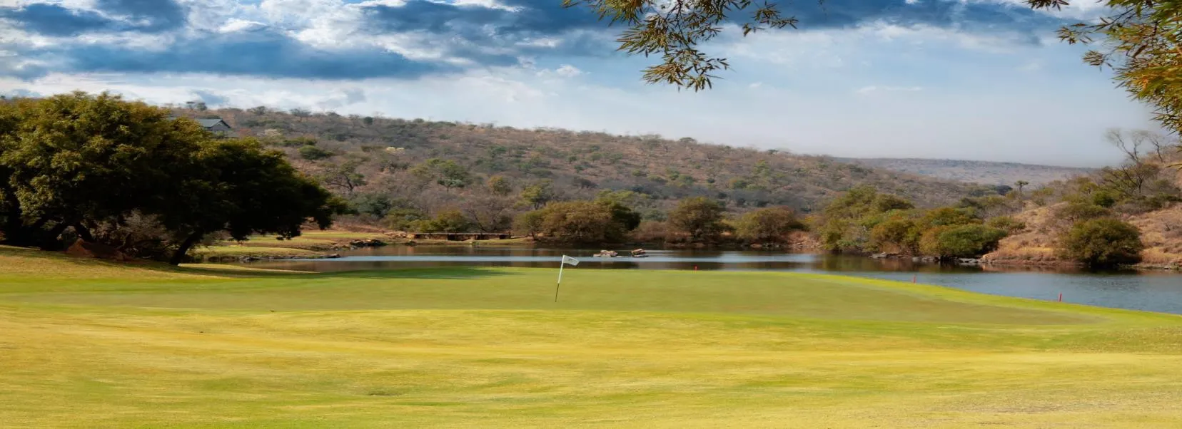 Golf course with a water hazard and trees under a partly cloudy sky