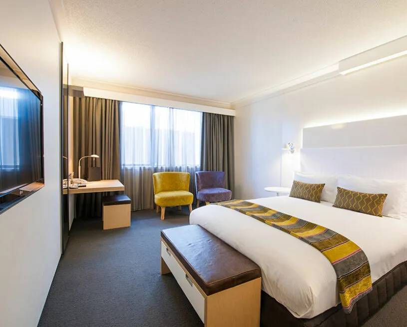 Modern hotel room with a large bed desk and armchair