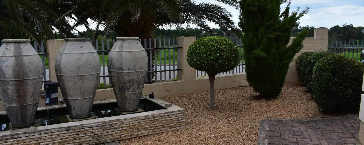 Three large stone urns in a garden with trimmed bushes and palm trees