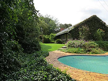 A house surrounded by greenery with a swimming pool in the foreground