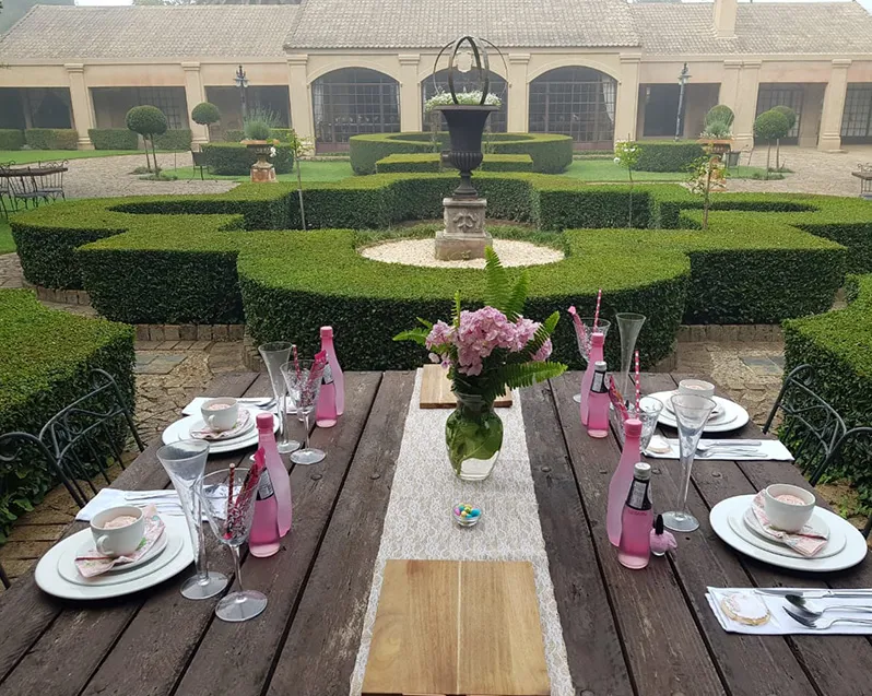 Outdoor table set with pink decorations and a garden with hedges in background