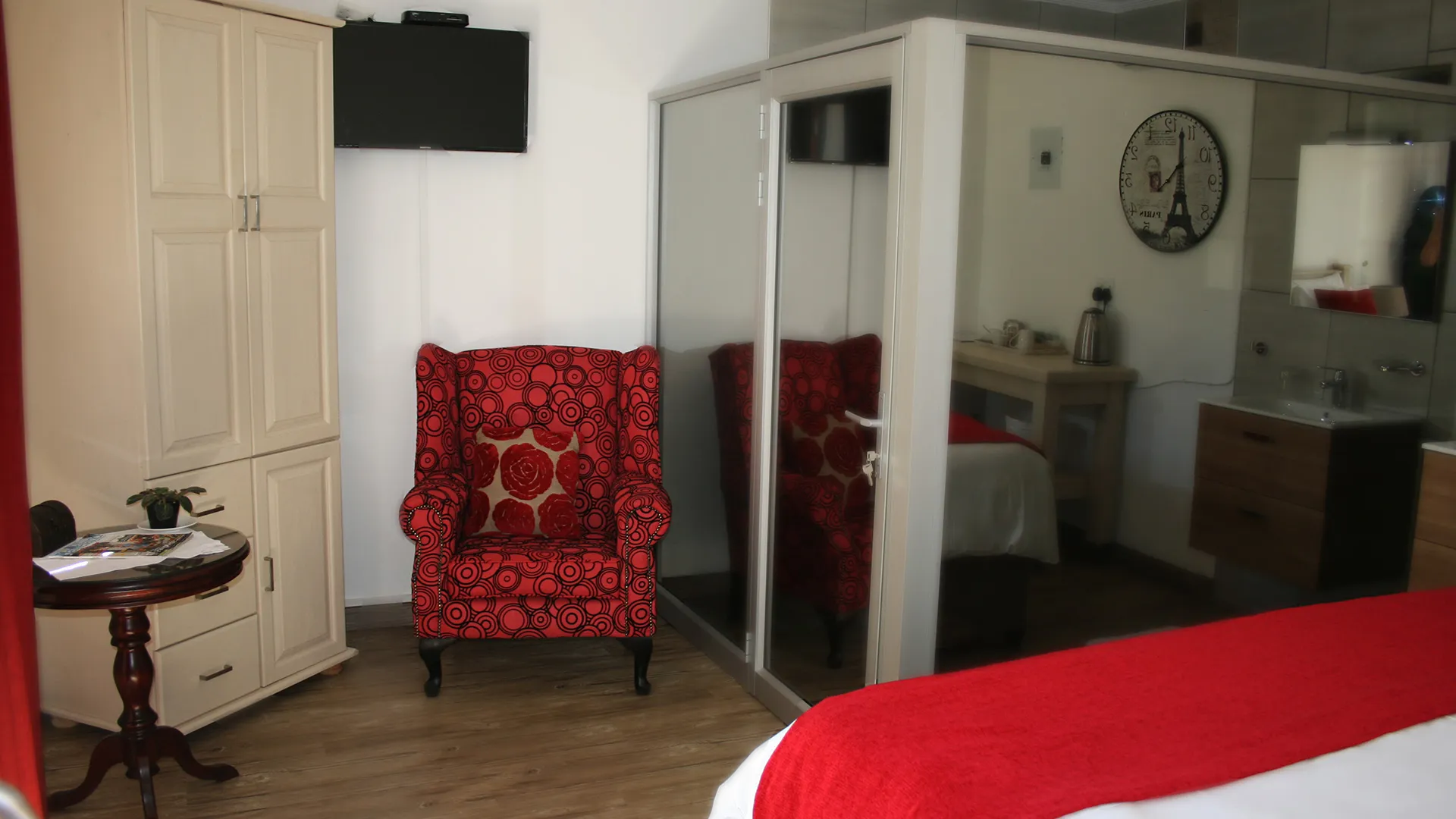 Bedroom with red chair wardrobe TV and ensuite bathroom reflection