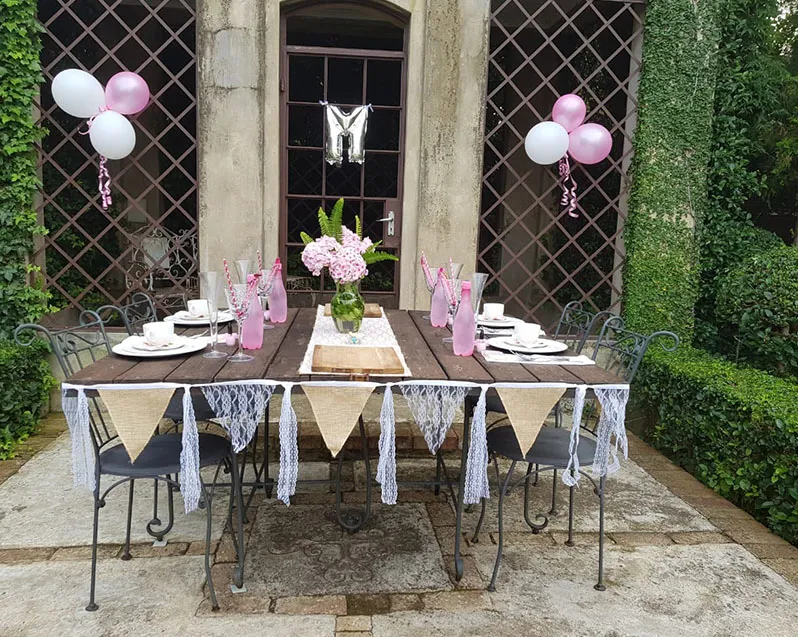 Outdoor table set for a party with pink and white decorations and balloons