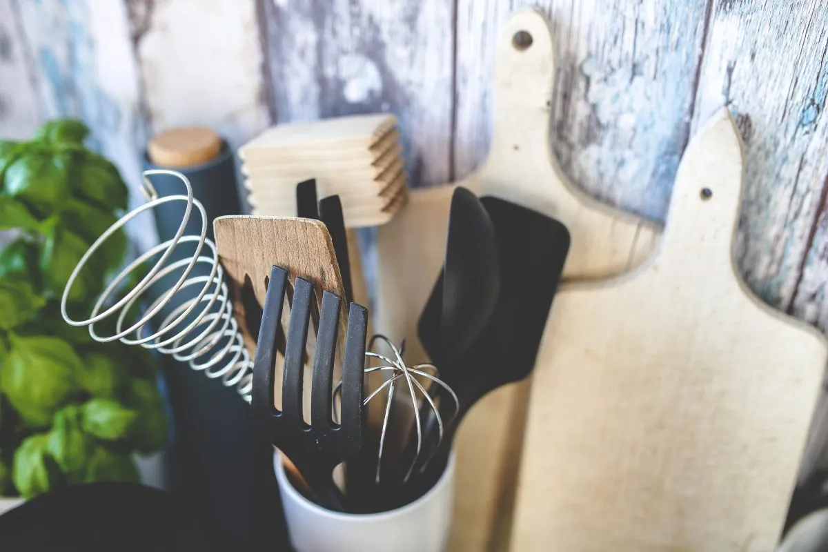 Various kitchen utensils and cutting boards against a wooden backdrop with plants