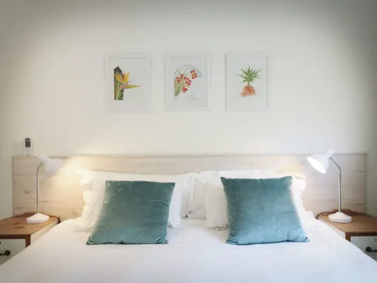 Bedroom with white bed teal pillows and three framed plant prints above