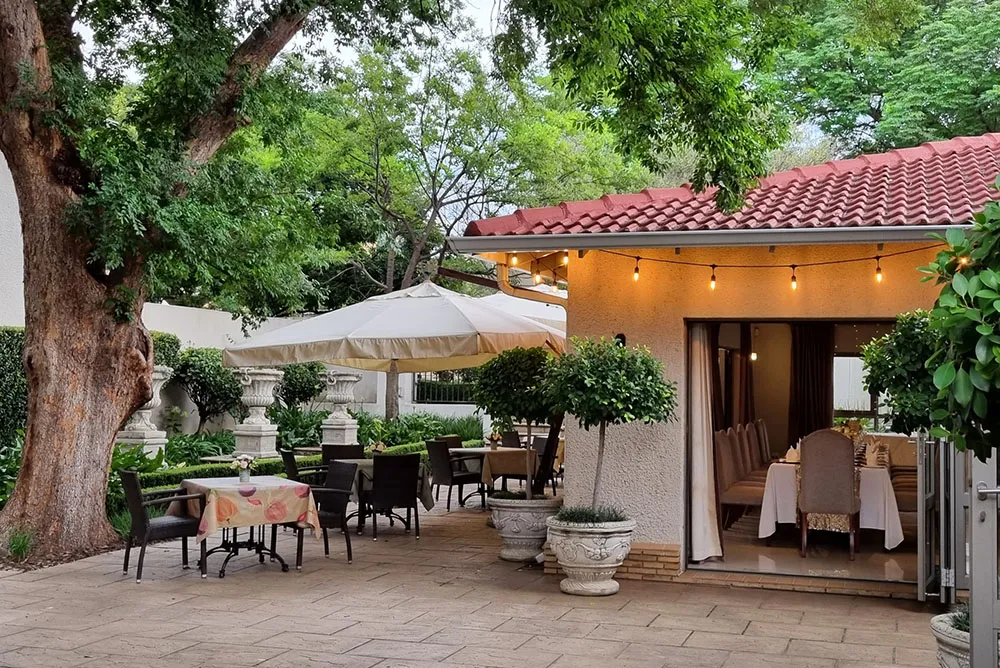 Outdoor dining area with tables chairs and umbrellas near a building with potted plants