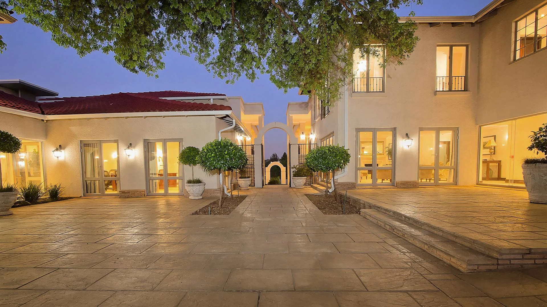 Modern courtyard with potted plants illuminated house and tiled pathway at night