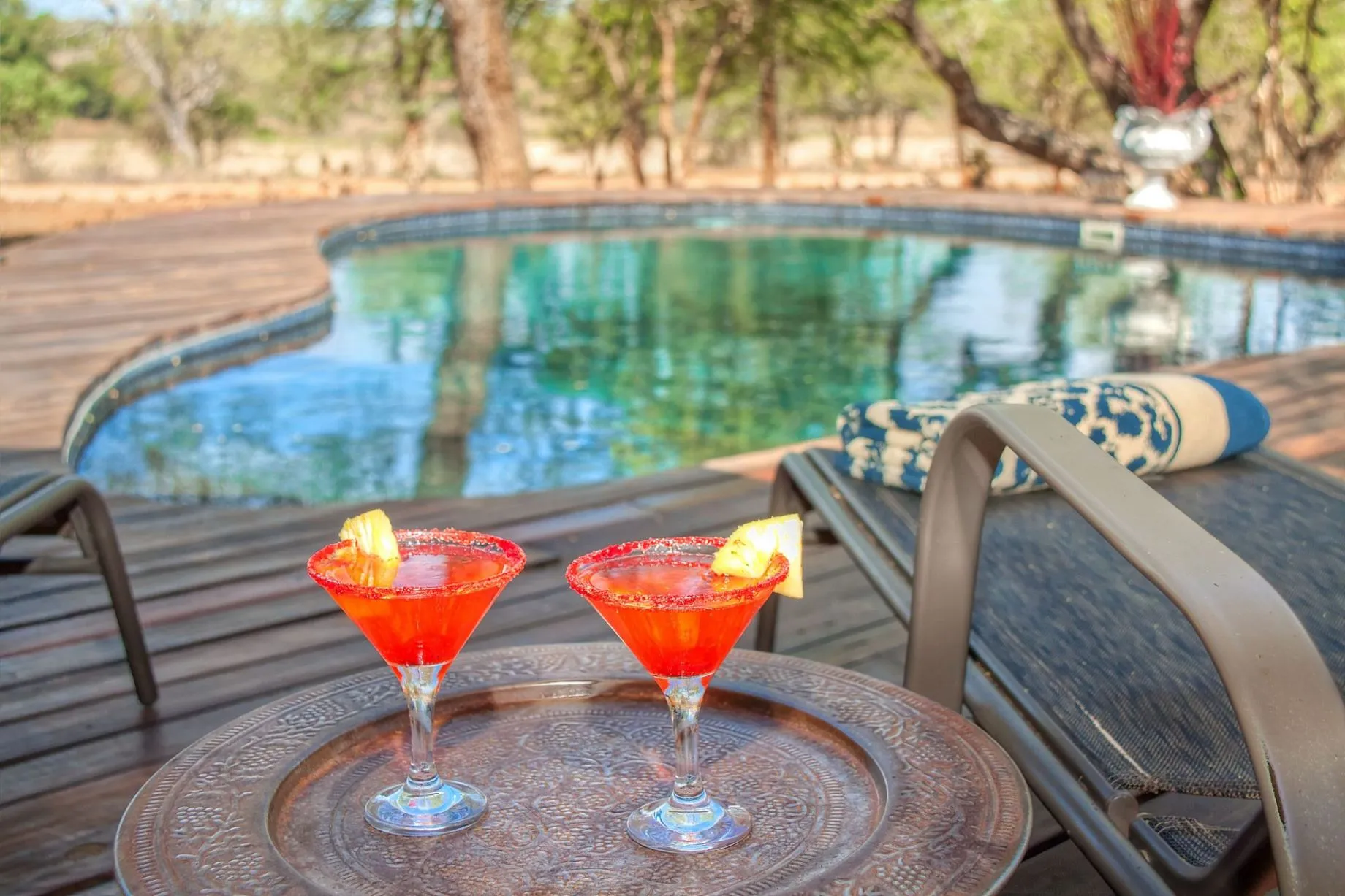 Two cocktails on a tray beside a pool with lounge chairs