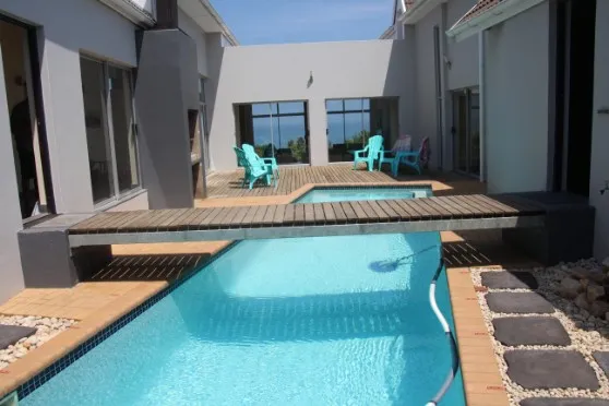 Swimming pool with wooden bridge and turquoise chairs in a modern courtyard