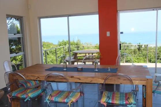 Wooden dining table with colorful chairs ocean view through large windows