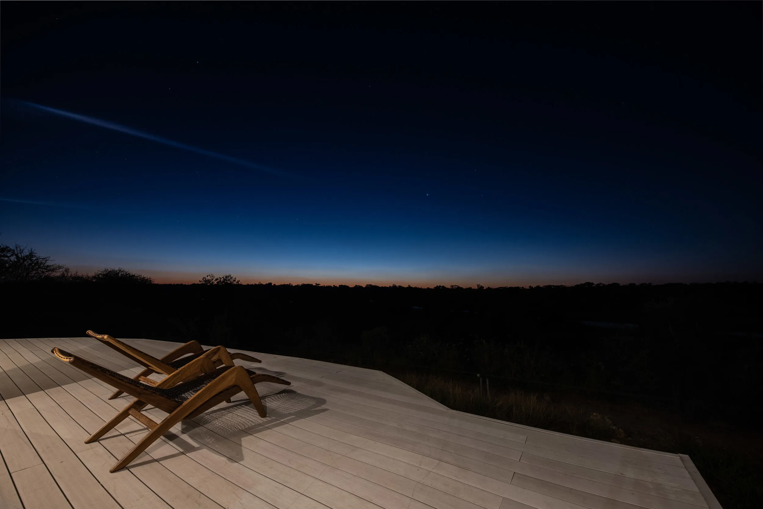 Two wooden chairs on a deck overlooking a dark starry night sky