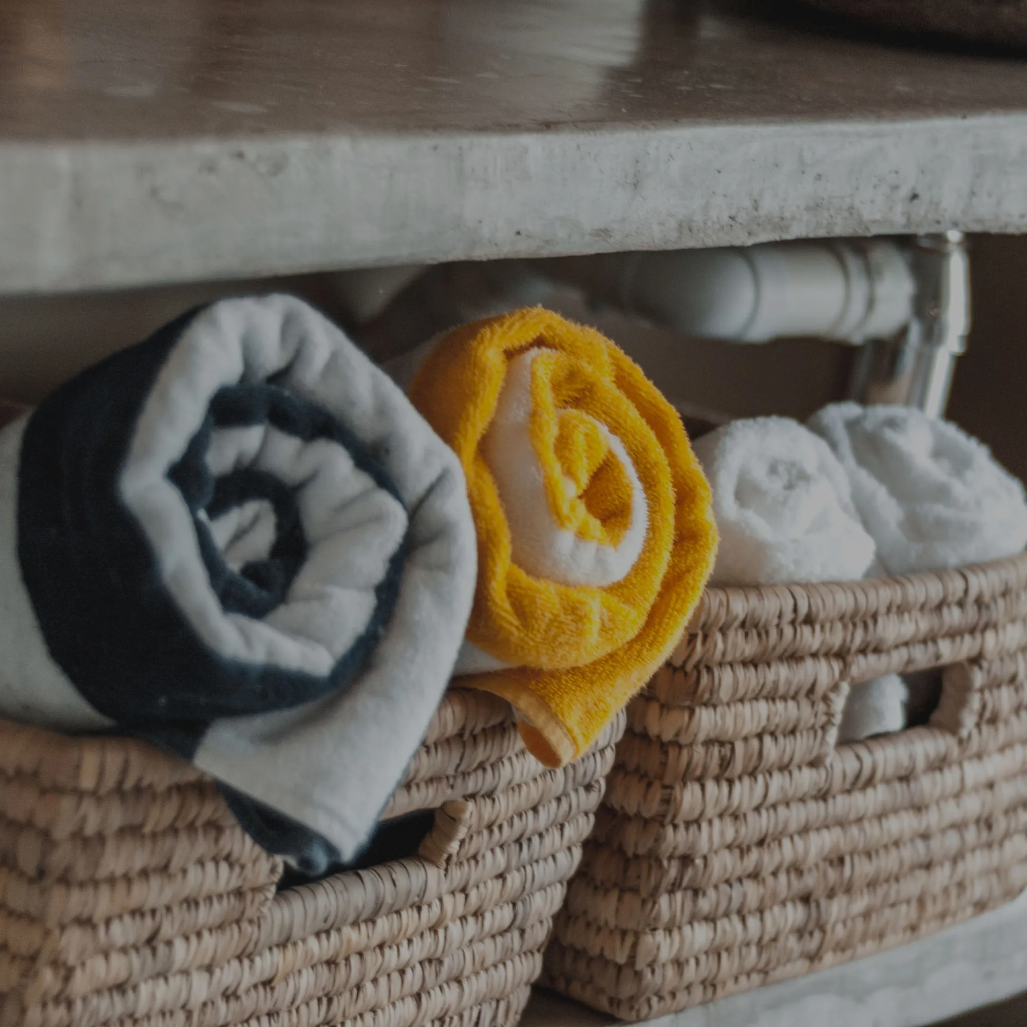 Two rolled towels in baskets on a shelf under a countertop