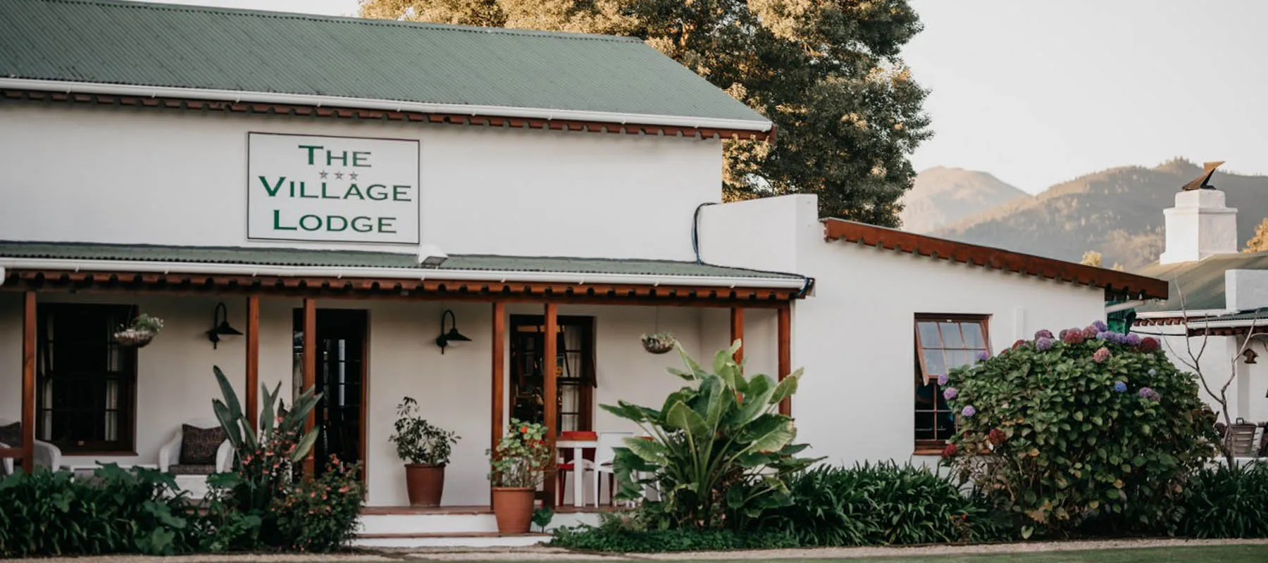 White building with green roof The Village Lodge sign surrounded by plants