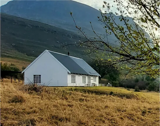 White house in grassy field with mountains in background and tree branches in foreground