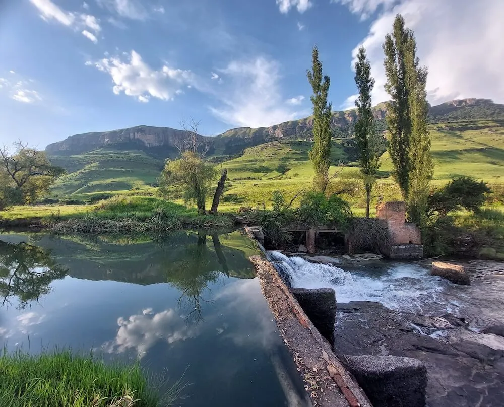 A serene pond with a small waterfall in a lush mountainous landscape