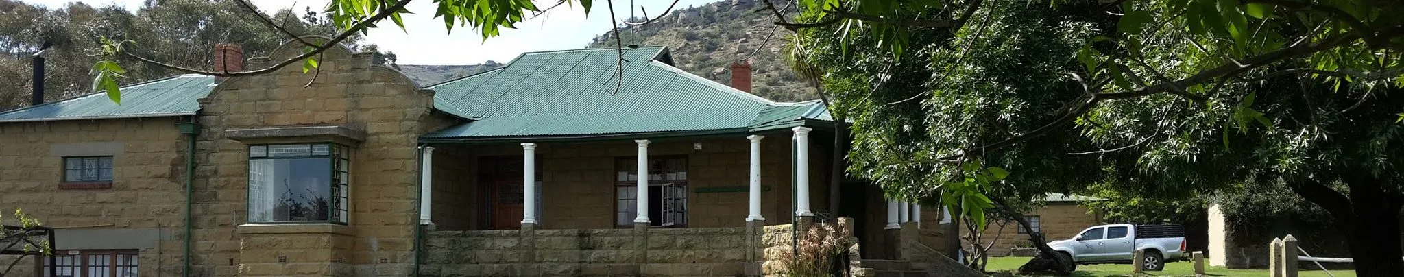 Stone house with green roof and large trees in a rural setting