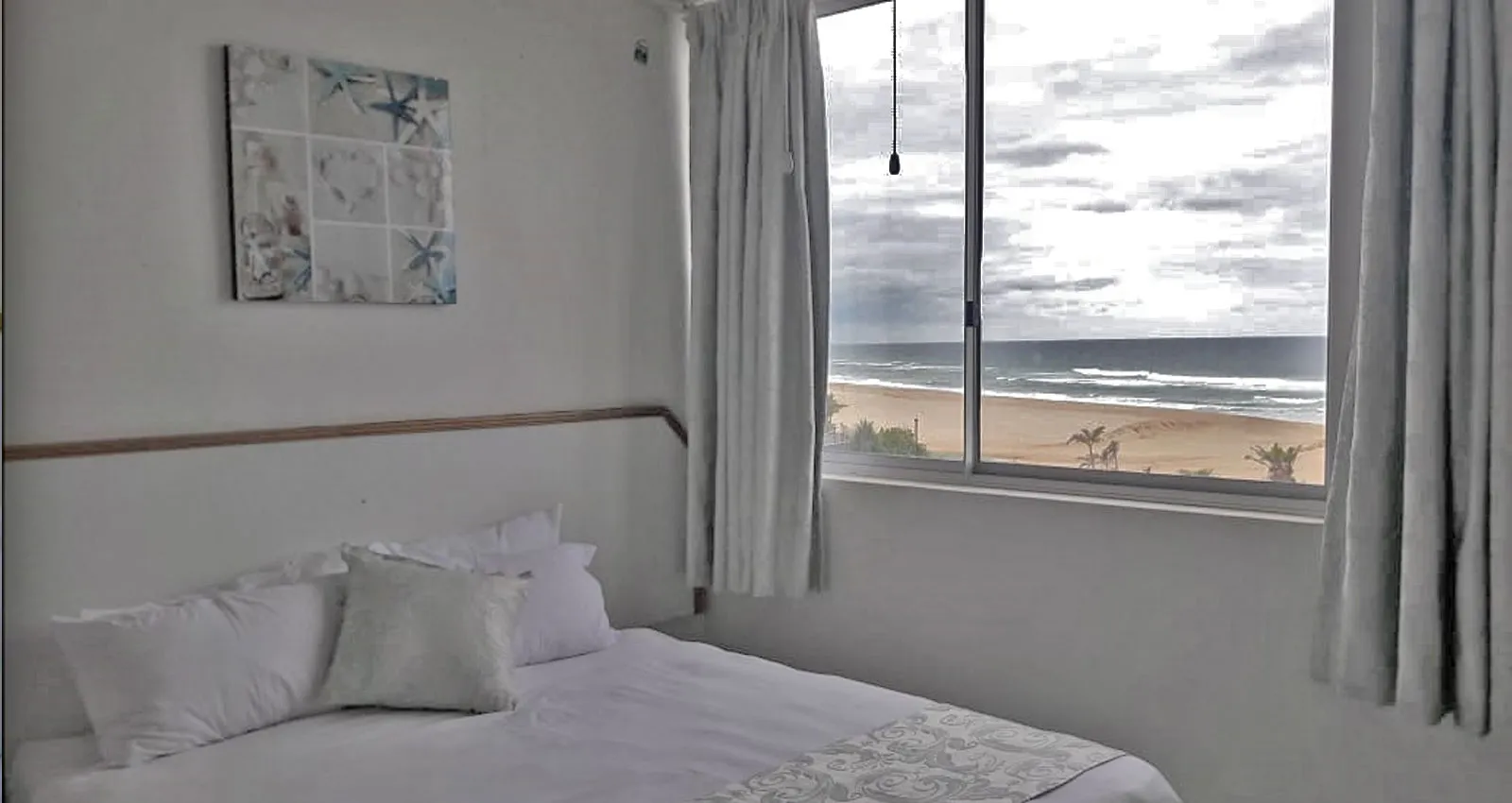Bedroom with a bed and large window overlooking a beach