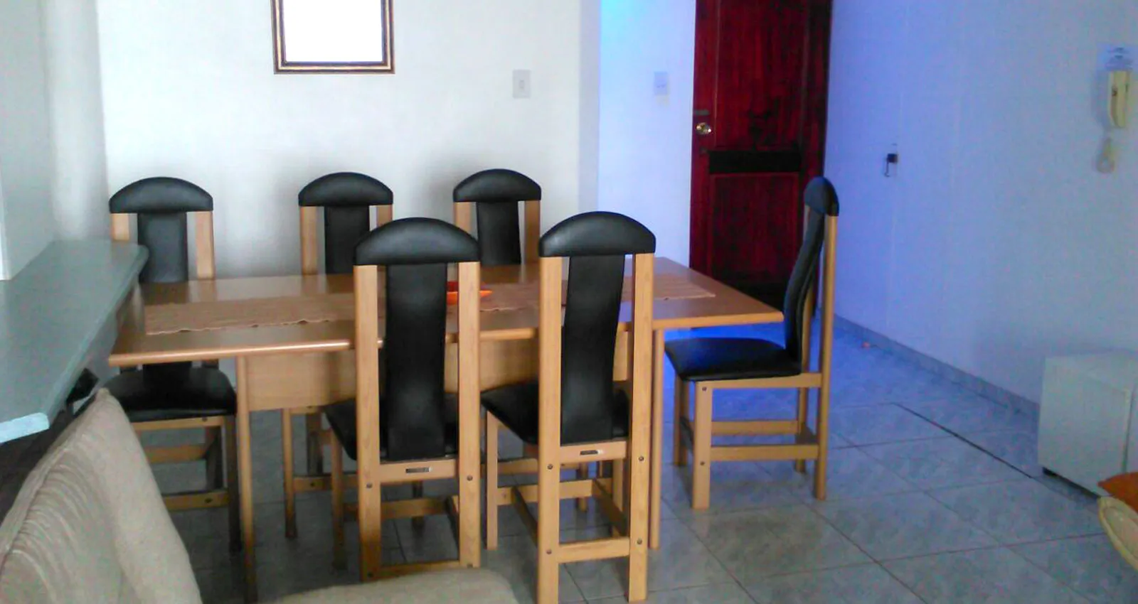 Dining area with wooden table six chairs and a red door in the background