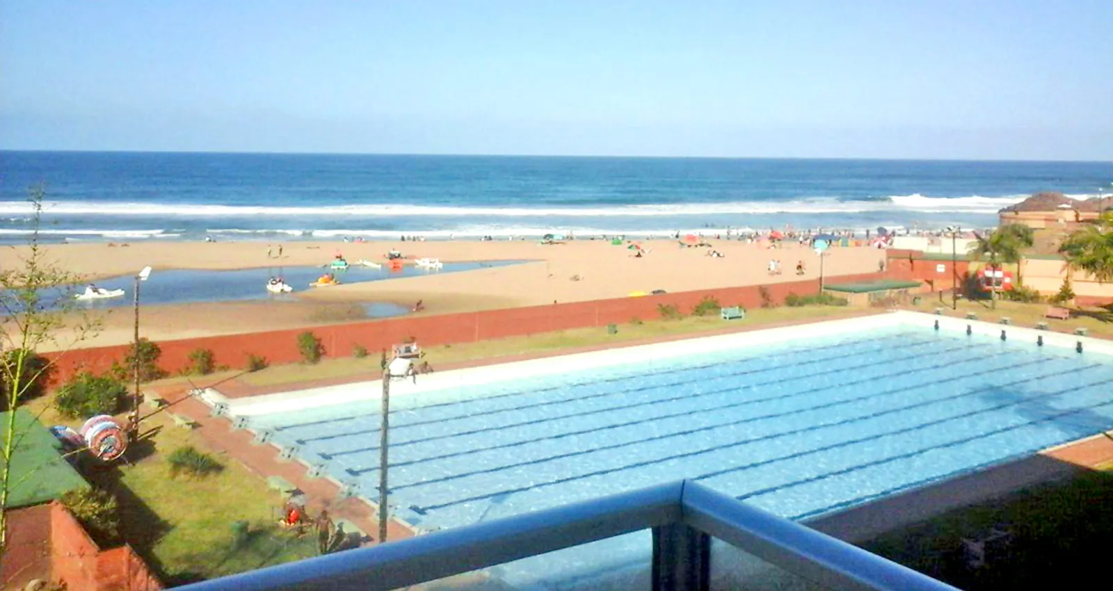 Swimming pool overlooking a beach with people enjoying the ocean and sand