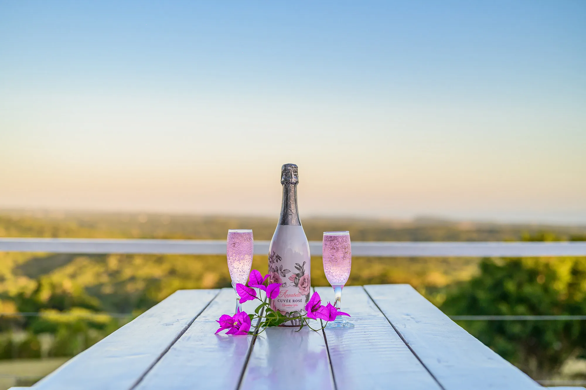 Two filled champagne glasses and a bottle on a wooden table with flowers