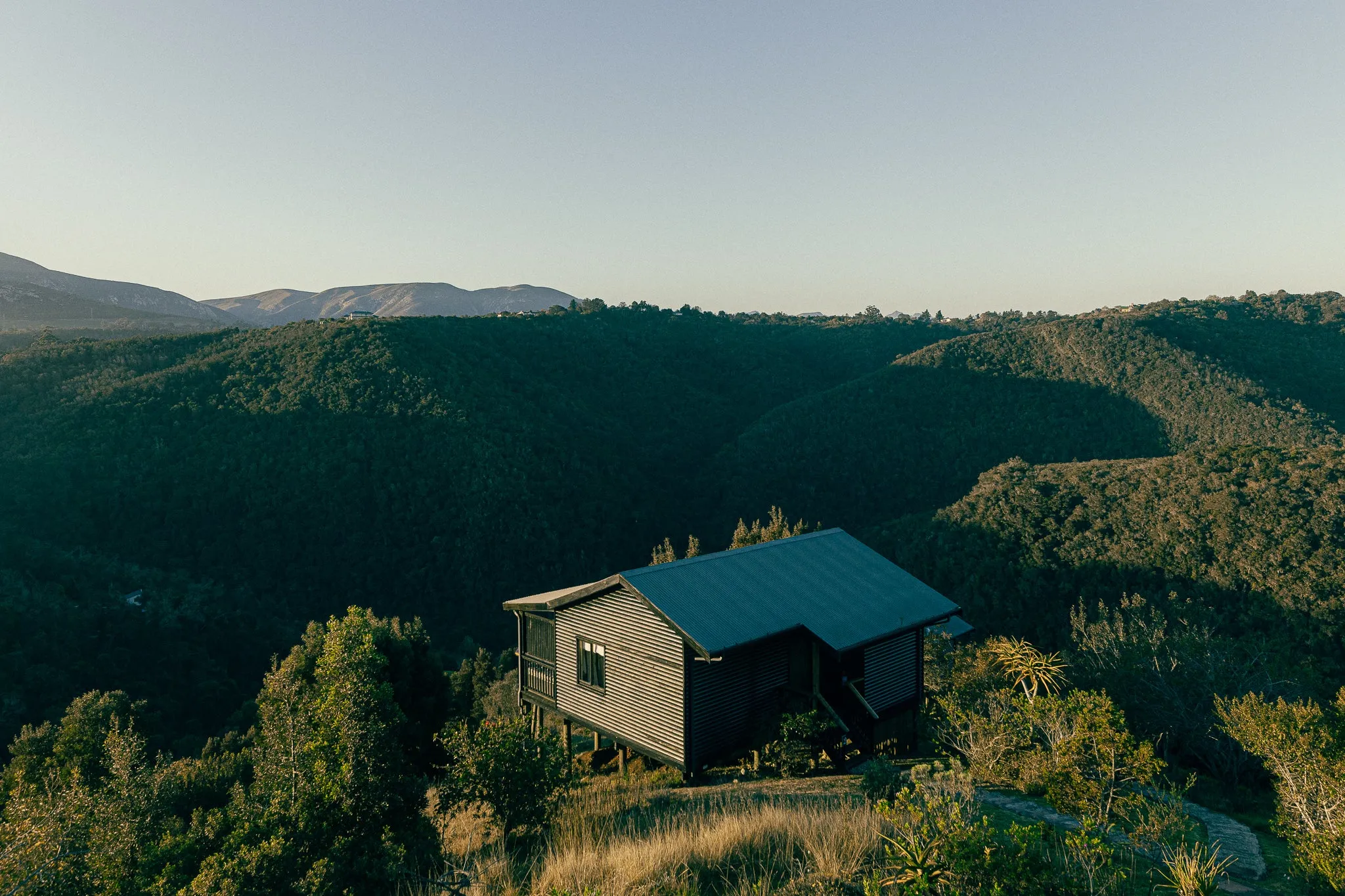 A cabin on a hill overlooking a forested valley and distant mountains