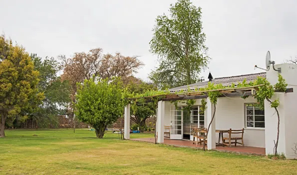 White house with a veranda surrounded by trees and a grassy lawn
