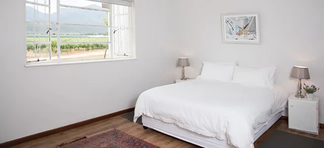 White bedroom with a large bed two bedside tables and a vineyard view
