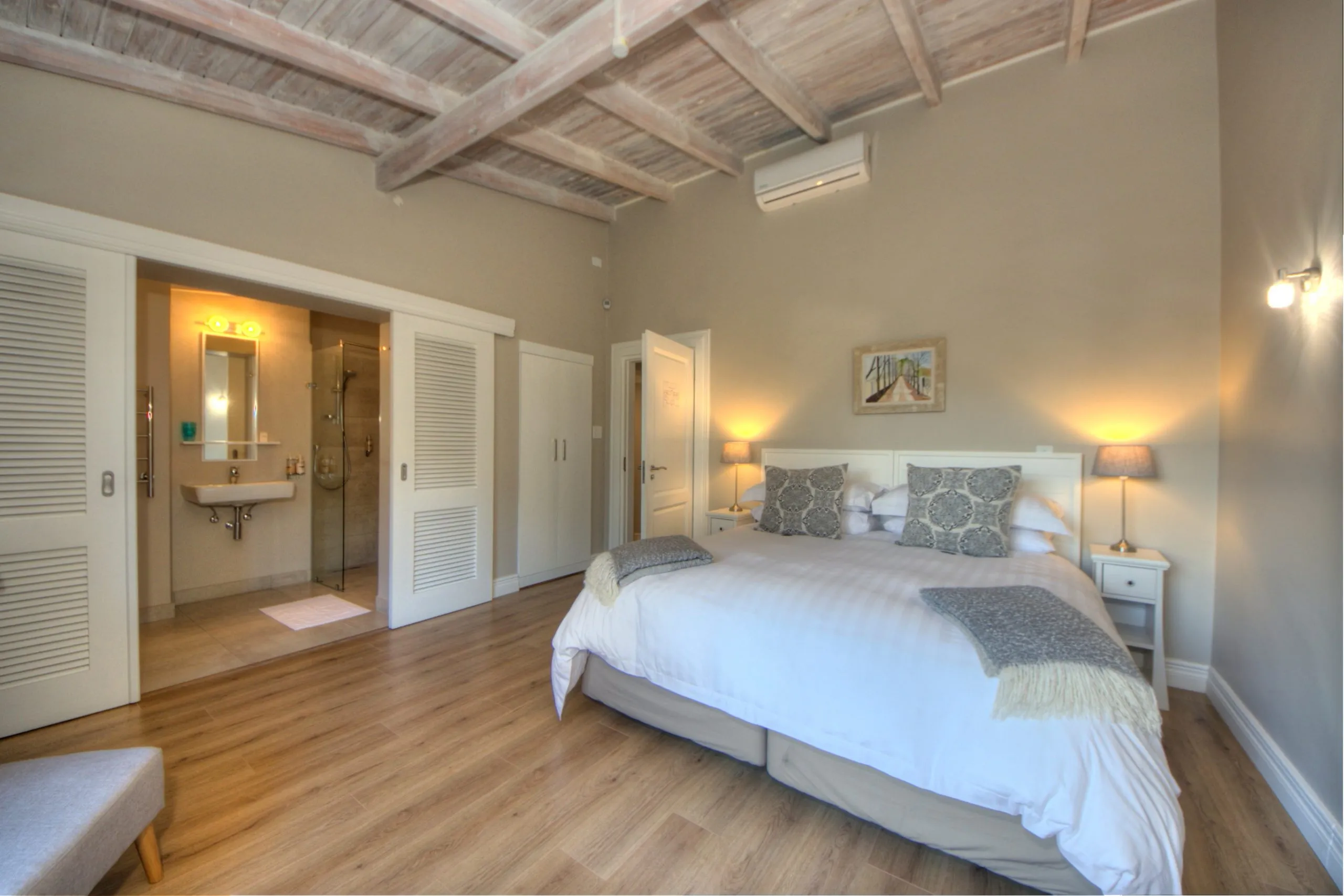 Bedroom with large bed wooden floor and adjacent bathroom with sink and mirror