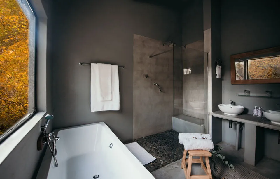 Modern bathroom with bathtub shower sink and large window showing autumn leaves