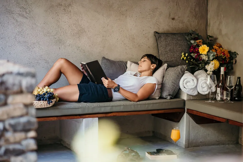 Person reading a book on a bench with flowers and drinks nearby