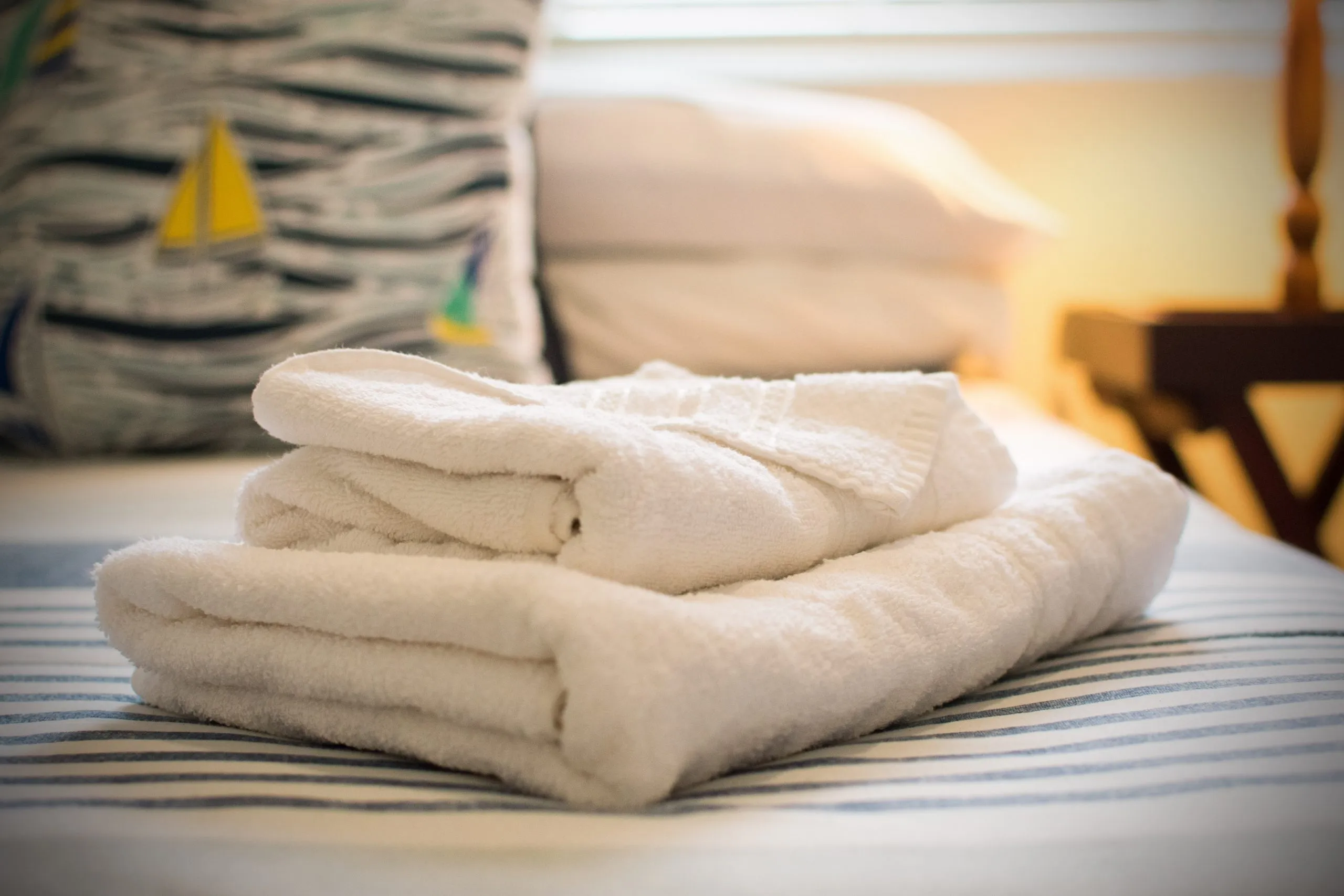 White towels on a bed with a nauticalthemed pillow in the background