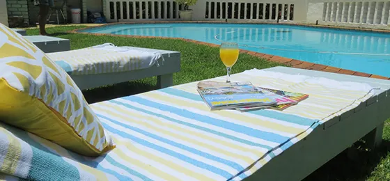 Two lounge chairs by a pool with a drink and magazines on one