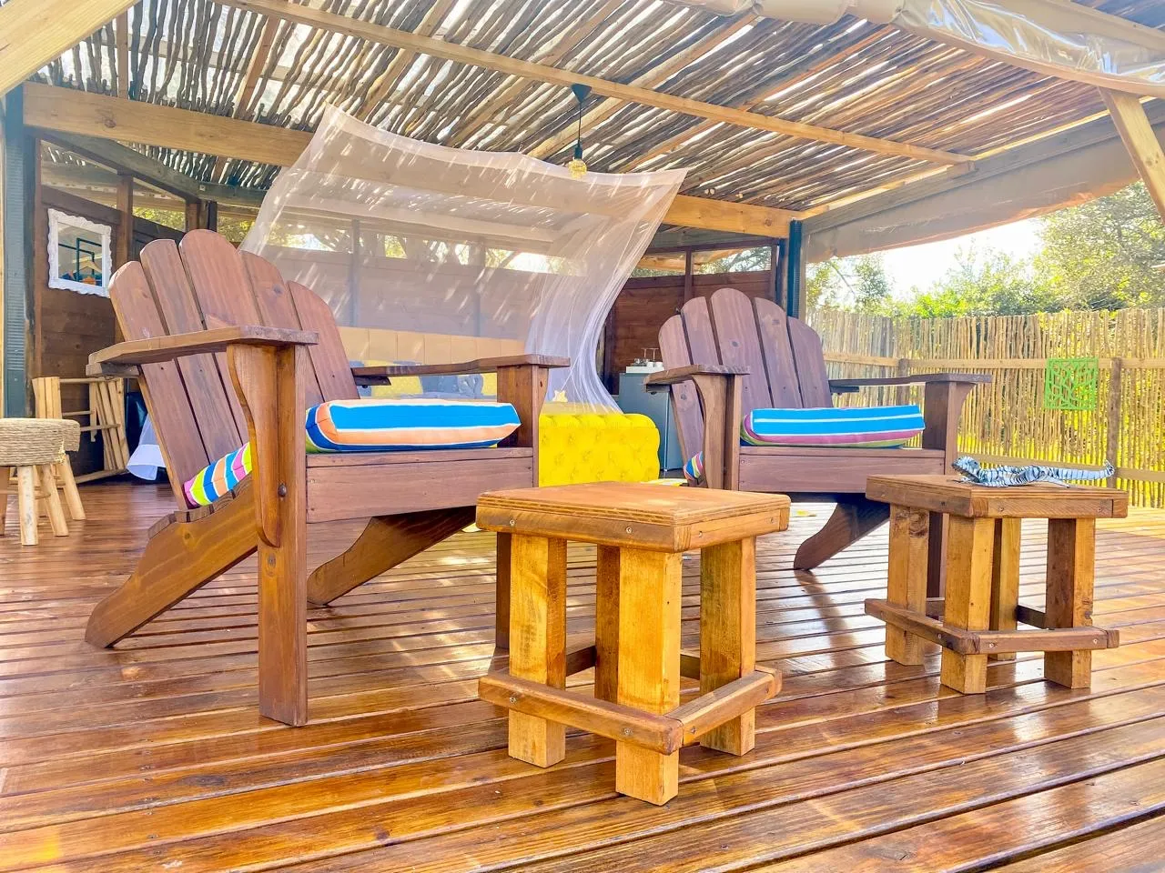 Two wooden chairs with colorful cushions under a thatched roof on a wooden deck