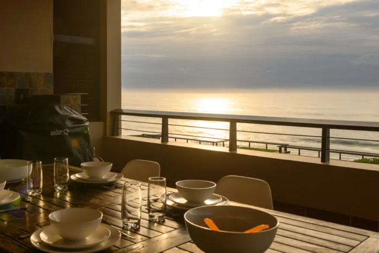 Outdoor dining table with bowls and glasses overlooking the ocean at sunset