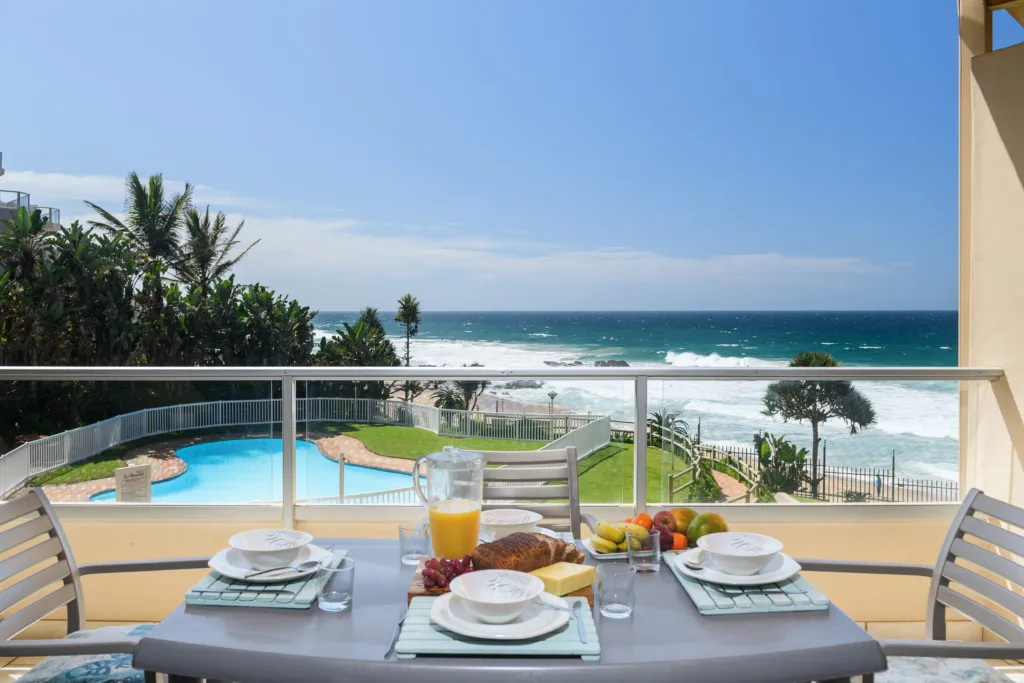 Breakfast table on balcony overlooking ocean and pool with blue sky