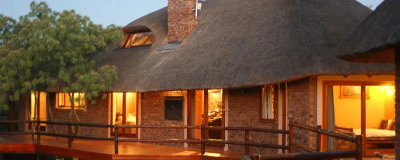 Cozy house with thatched roof and wooden deck warmly lit at dusk