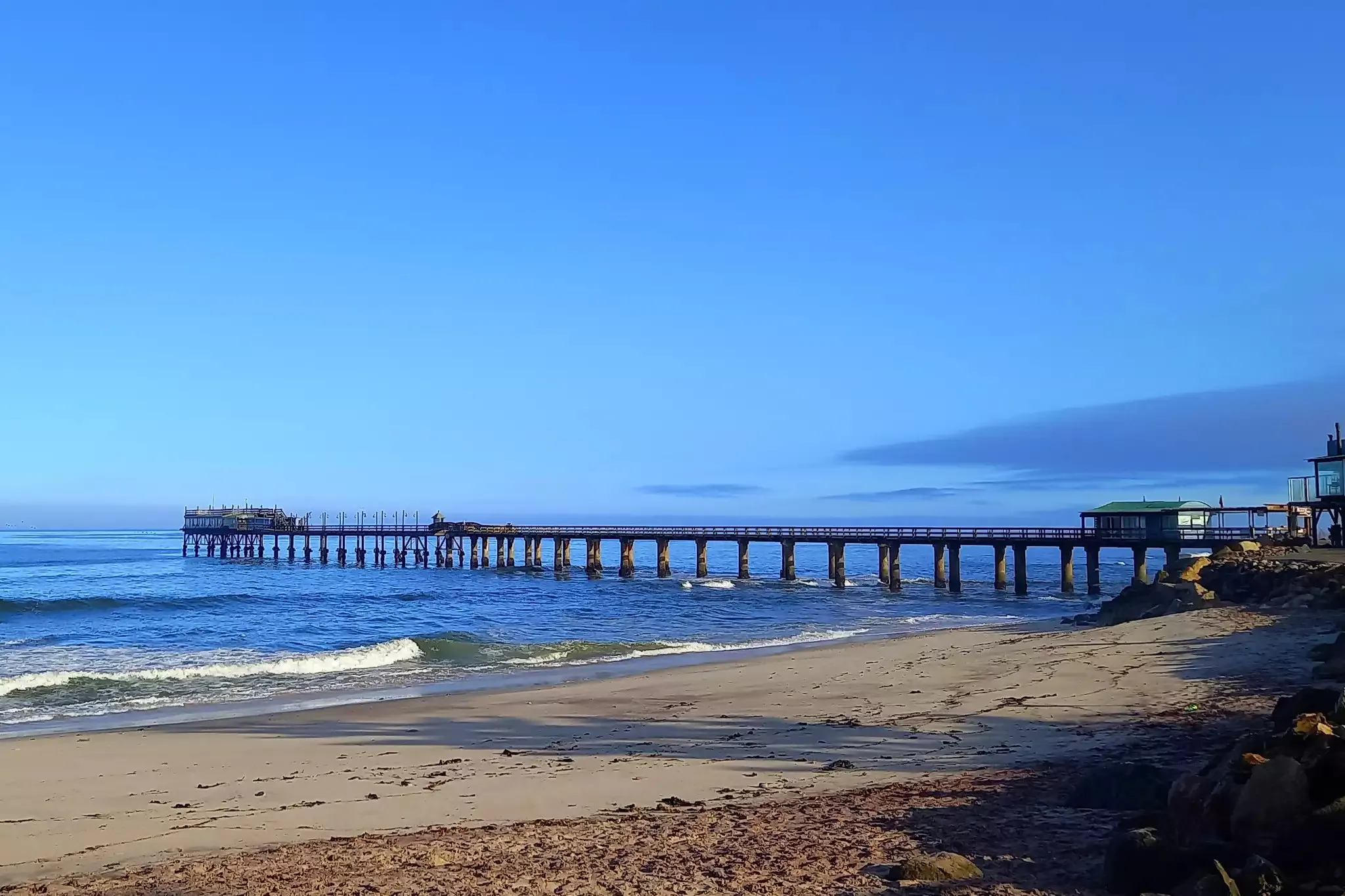 Beach with waves pier extending into the ocean clear blue sky