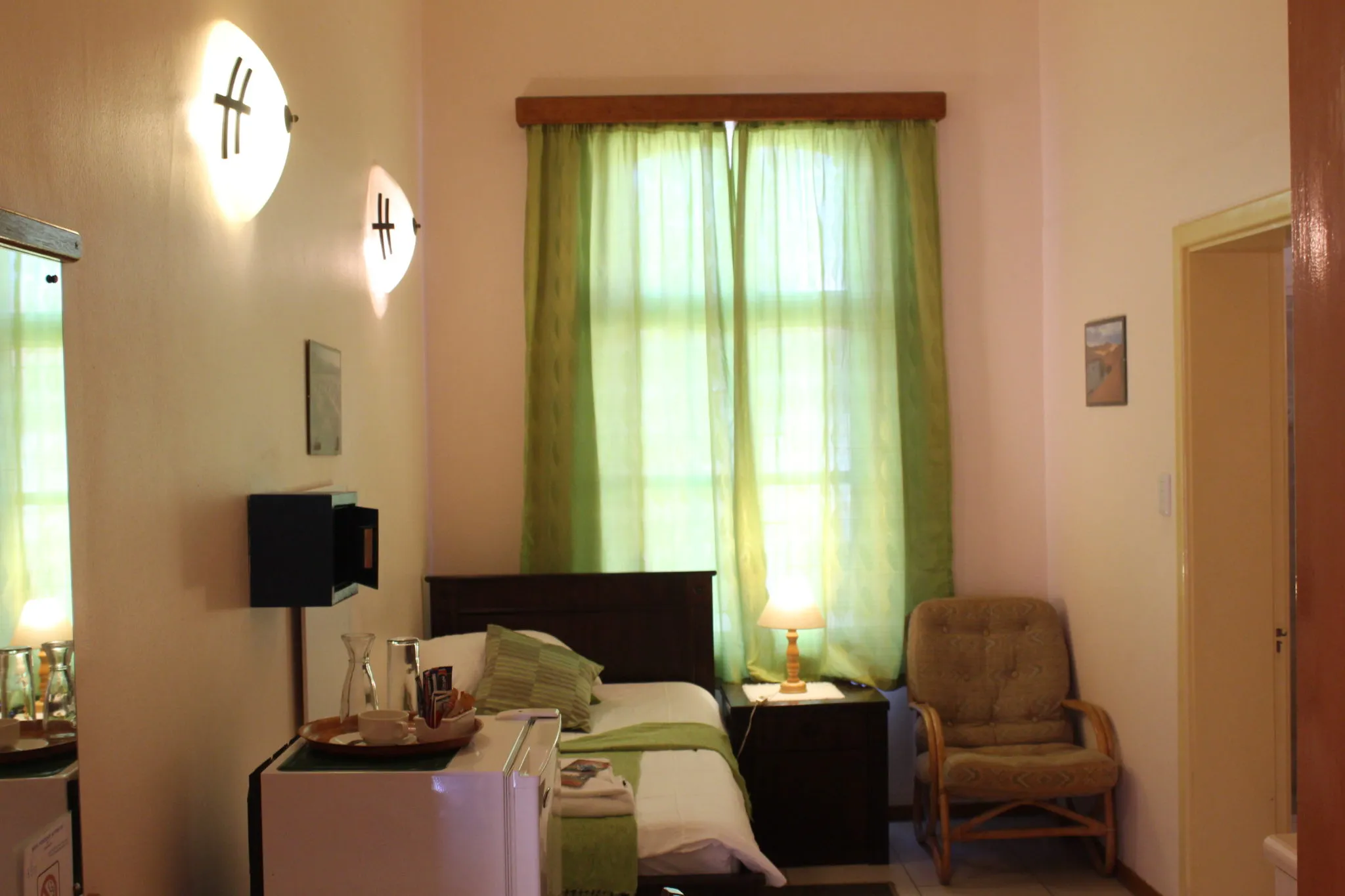 Cozy bedroom with green curtains bed armchair and window letting in sunlight