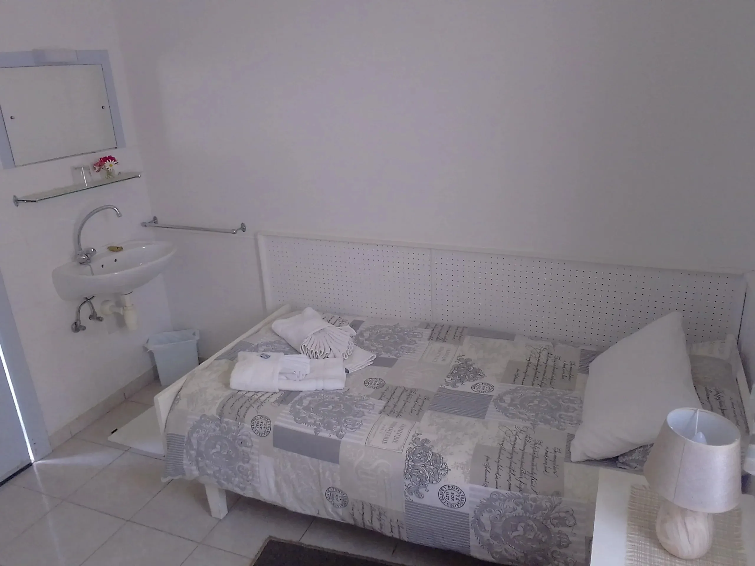 Small bedroom with single bed sink and bedside table with lamp