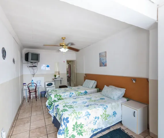 Two single beds in a tidy whitewalled bedroom with a ceiling fan