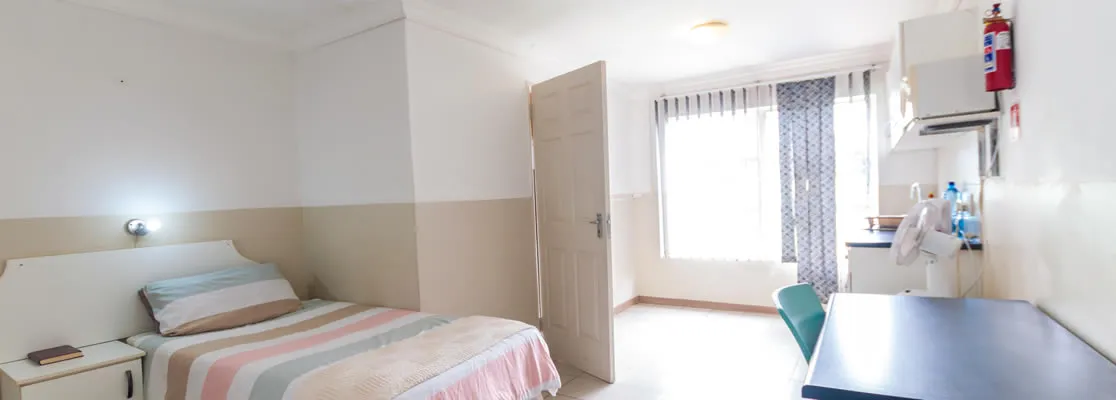 Small bedroom with bed desk window with curtains and open door