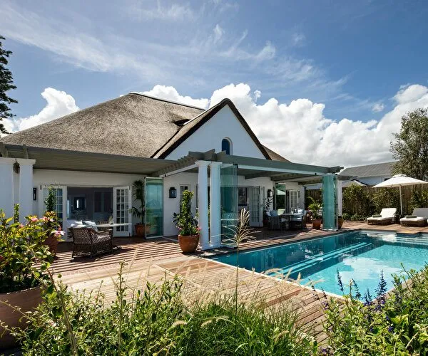 Modern house with thatched roof pool and garden furniture under blue sky