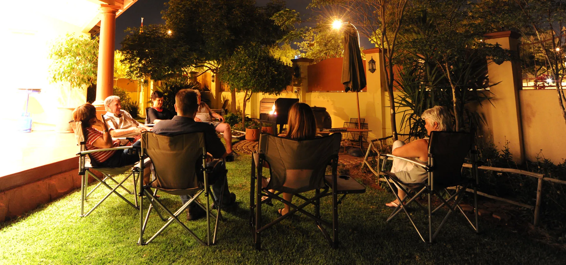 Group of people sitting in camp chairs outdoors at night under trees