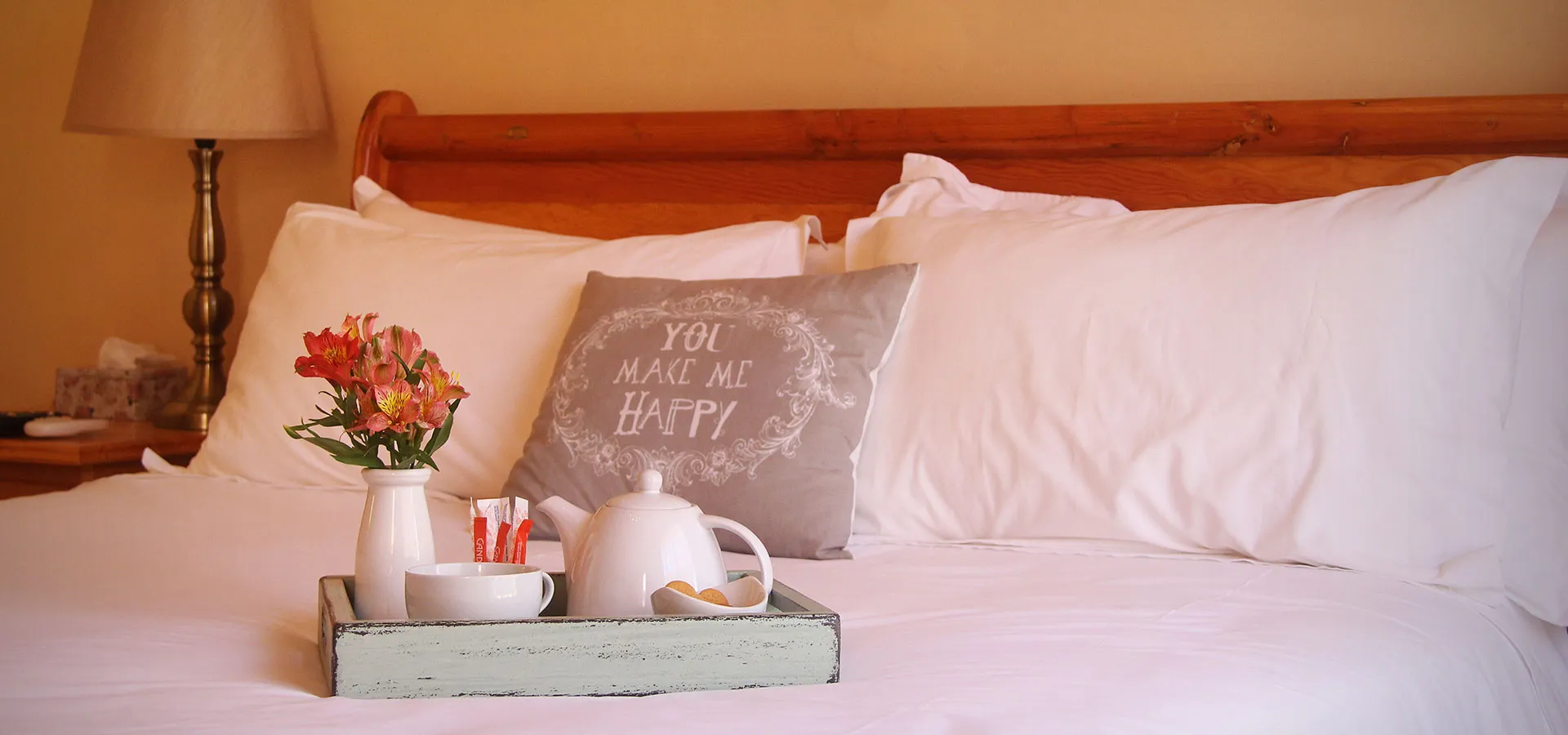 Wooden bed with pillows tray holding flowers teapot and cup on white sheets