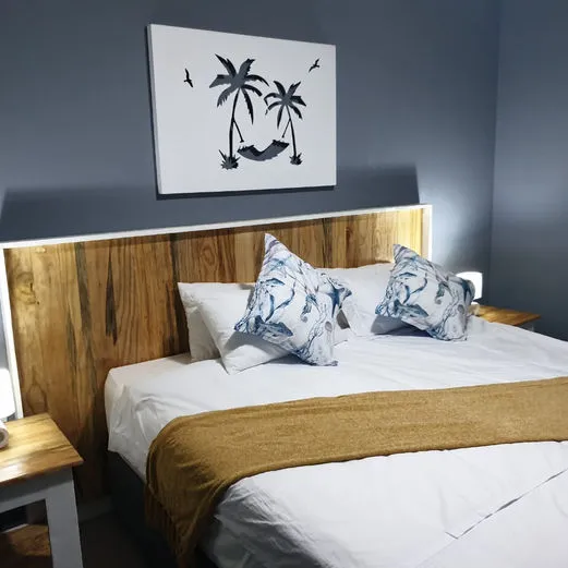 Wooden headboard palm tree art white bedding and yellow throw blanket on bed