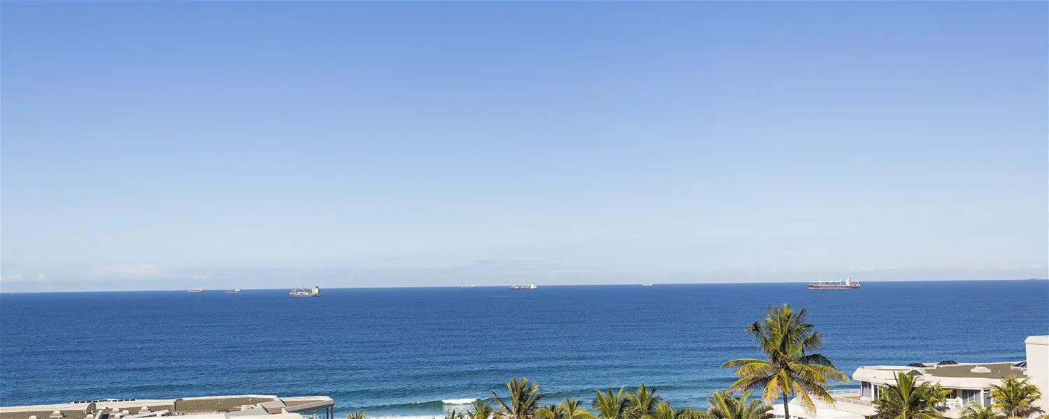 Ocean view with palm trees buildings and distant ships under a clear blue sky