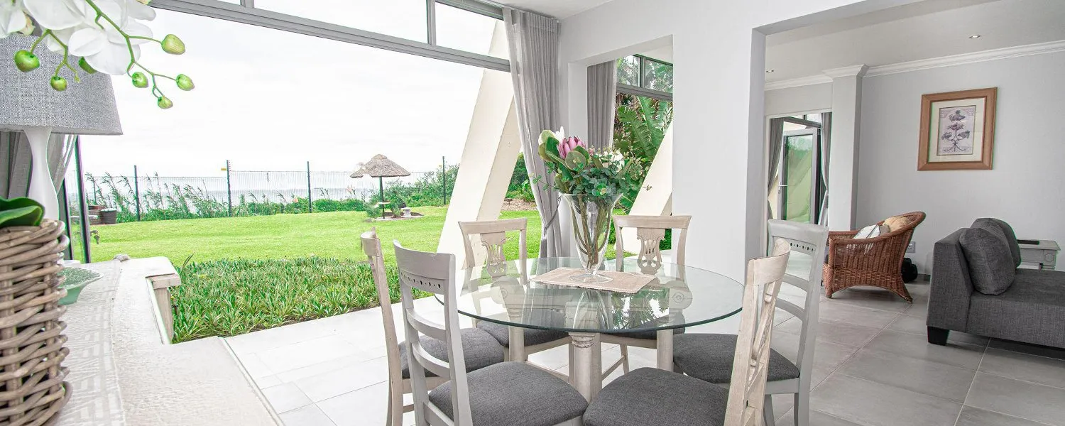 Dining area with glass table and chairs adjacent to living room with garden view