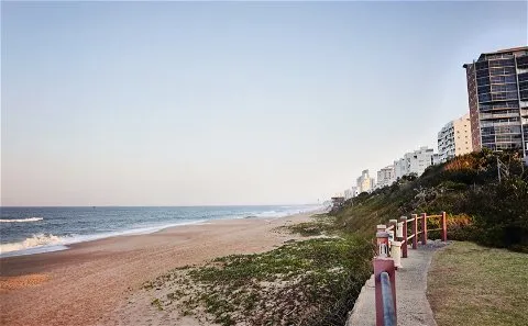 Beach with sandy shore ocean waves and buildings along a pathway