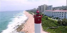 Lighthouse overlooking a sandy beach with waves and buildings in the background