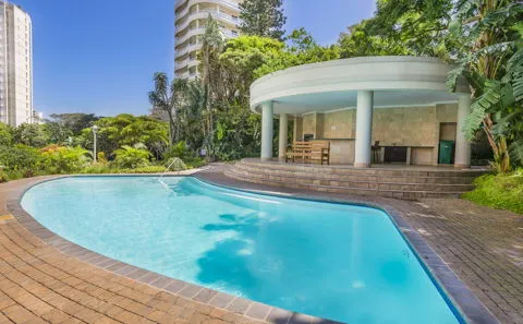 Swimming pool with gazebo surrounded by greenery and tall buildings in the background